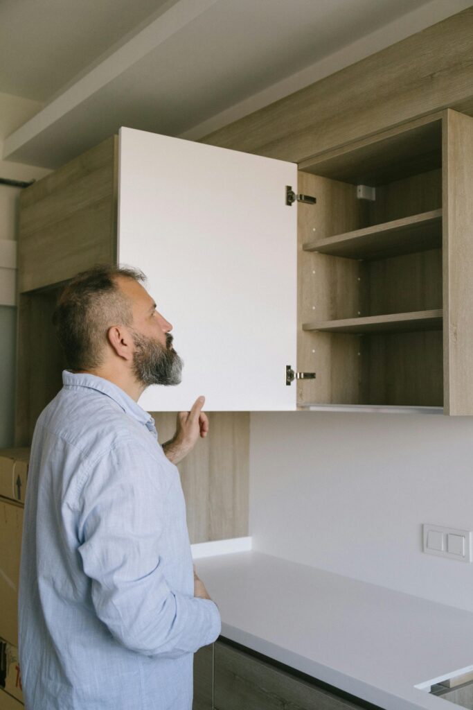 Bearded man in a blue shirt checking a kitchen cabinet in a modern indoor setting.